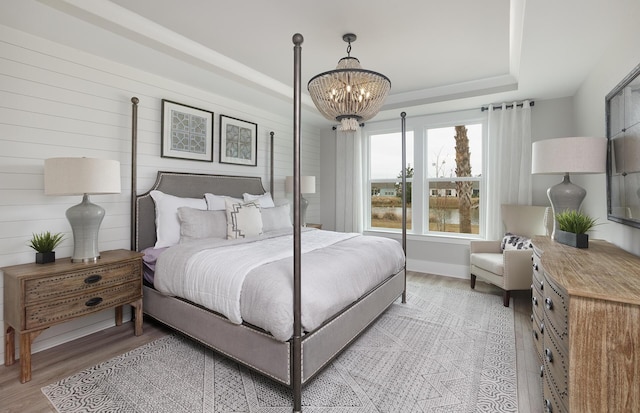 bedroom featuring baseboards, a chandelier, light wood-type flooring, and a raised ceiling