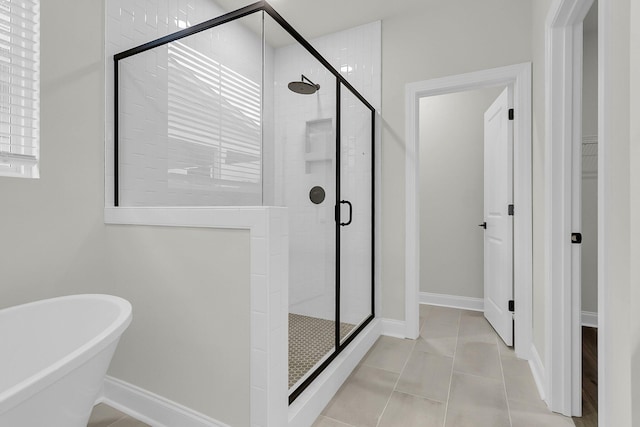 full bathroom featuring a stall shower, baseboards, a freestanding bath, and tile patterned floors