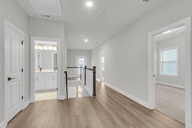 corridor featuring light wood-style floors, attic access, visible vents, and an upstairs landing