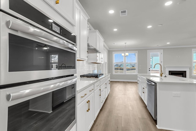 kitchen with stainless steel appliances, white cabinets, light countertops, tasteful backsplash, and crown molding