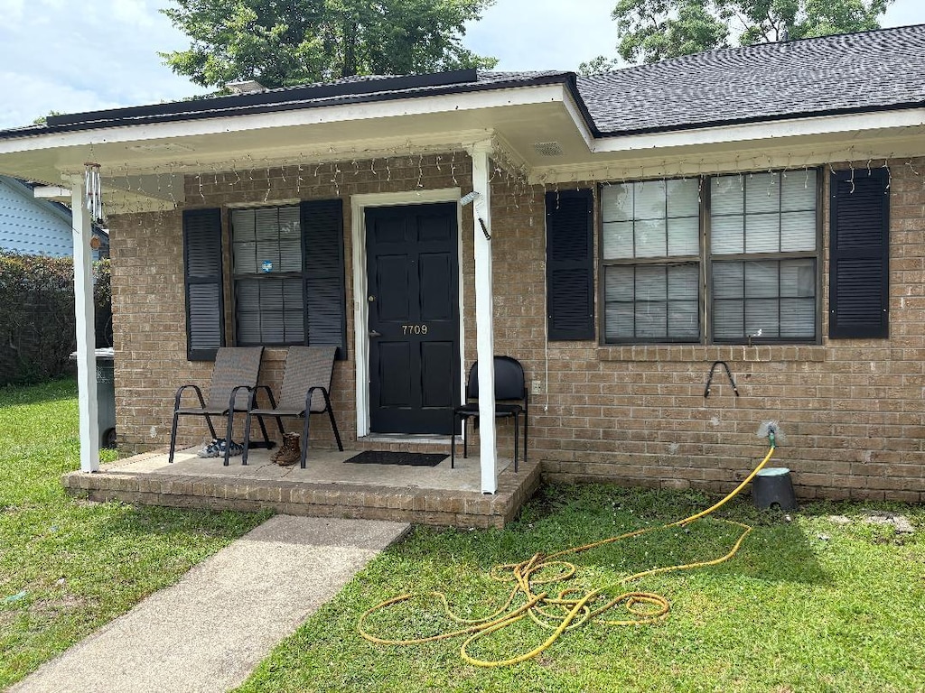 7709 Suzanne Dr, North Charleston, SC 29418 - doorway to property featuring covered porch, brick siding, and a yard