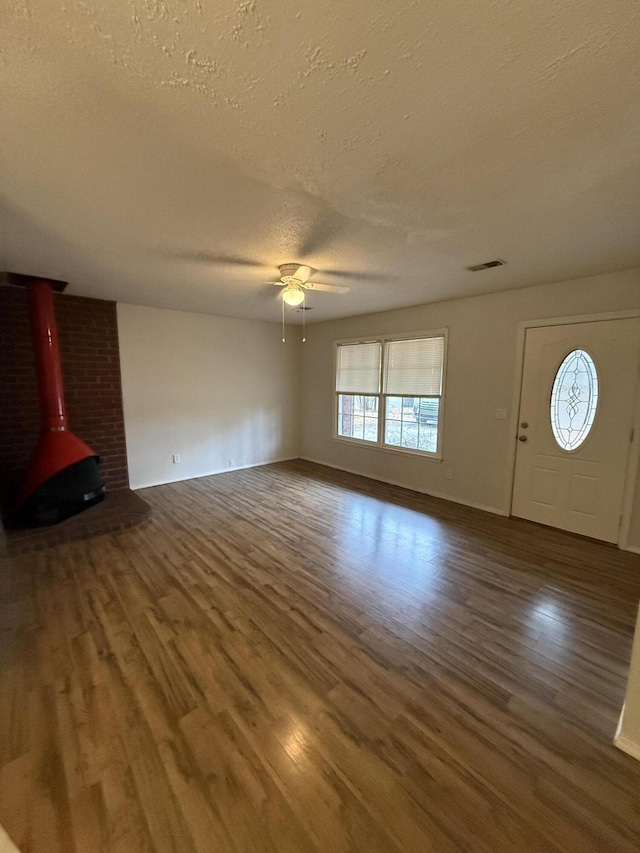 unfurnished living room featuring a textured ceiling, hardwood / wood-style flooring, a wood stove, and ceiling fan