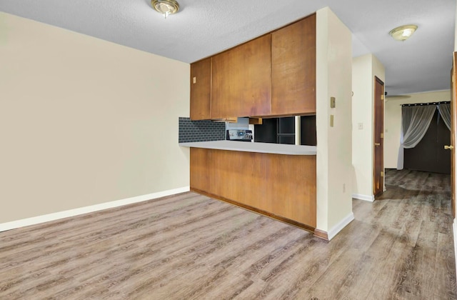 kitchen with black refrigerator, light wood-type flooring, a textured ceiling, tasteful backsplash, and kitchen peninsula