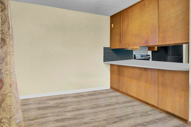 kitchen featuring decorative backsplash, black fridge, light hardwood / wood-style floors, and a textured ceiling