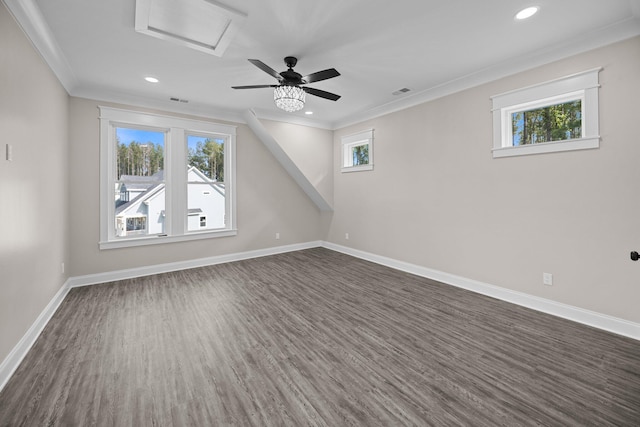empty room with dark wood-type flooring, ornamental molding, plenty of natural light, attic access, and baseboards