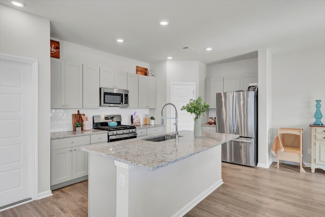 kitchen featuring sink, appliances with stainless steel finishes, light wood-type flooring, and an island with sink