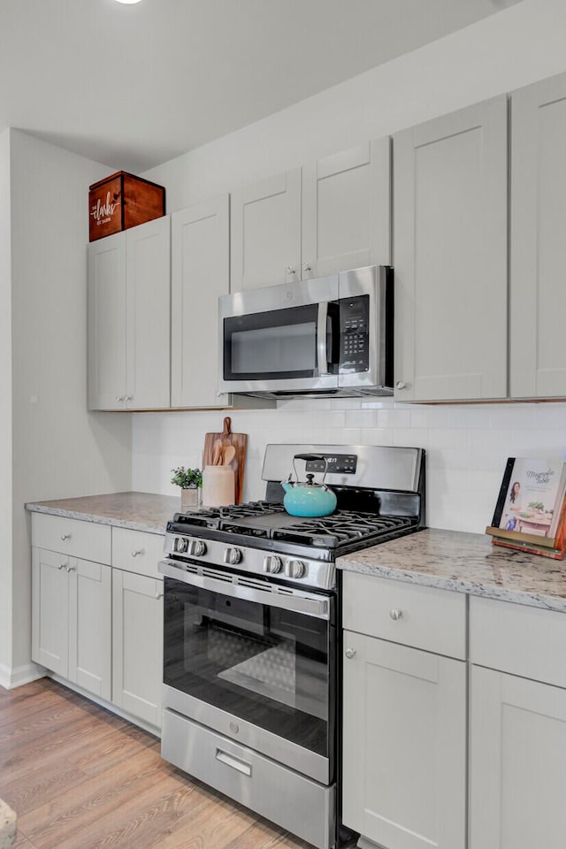 kitchen featuring tasteful backsplash, appliances with stainless steel finishes, light wood-type flooring, white cabinets, and light stone counters