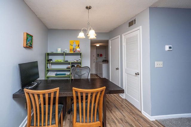 dining space featuring visible vents, baseboards, a chandelier, wood finished floors, and washer and dryer