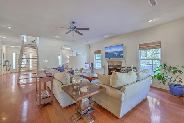 living room featuring visible vents, arched walkways, a warm lit fireplace, ceiling fan, and hardwood / wood-style flooring