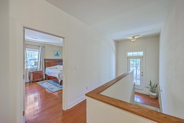 hallway with an upstairs landing, wood finished floors, and baseboards