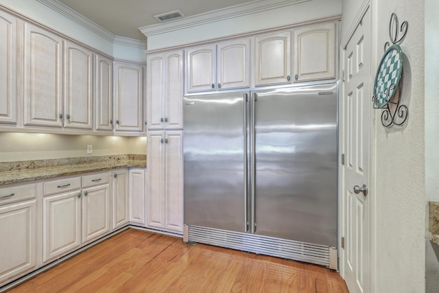 kitchen with visible vents, built in fridge, crown molding, light wood finished floors, and light stone countertops