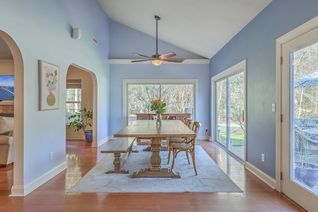 dining space with arched walkways, baseboards, a ceiling fan, and wood finished floors