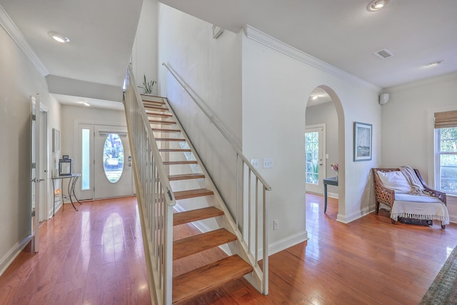 stairway with visible vents, baseboards, ornamental molding, wood finished floors, and arched walkways