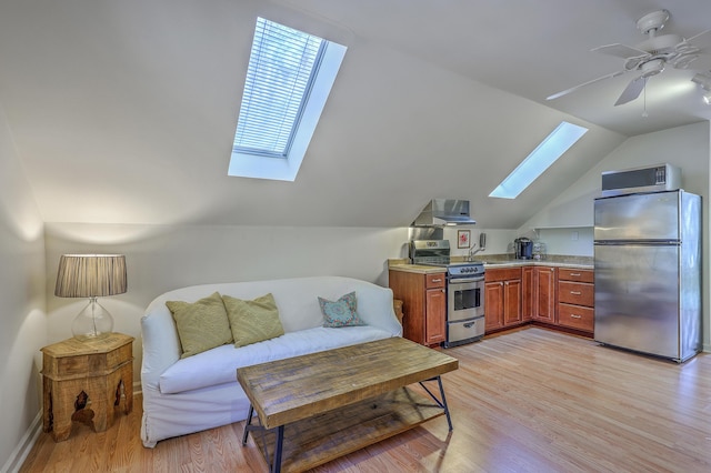 sitting room featuring lofted ceiling with skylight, baseboards, light wood-type flooring, and ceiling fan