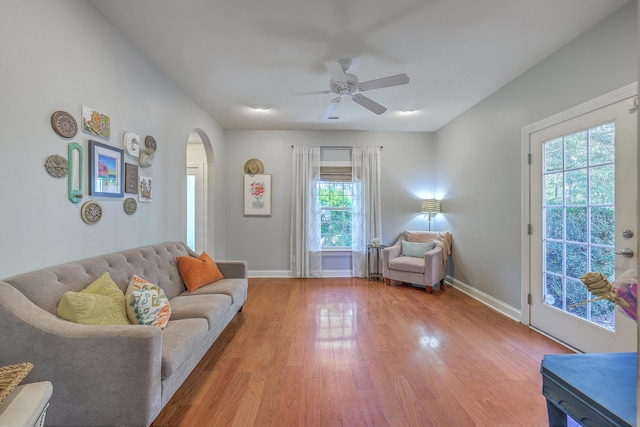 living area with light wood-style flooring, a ceiling fan, baseboards, and arched walkways