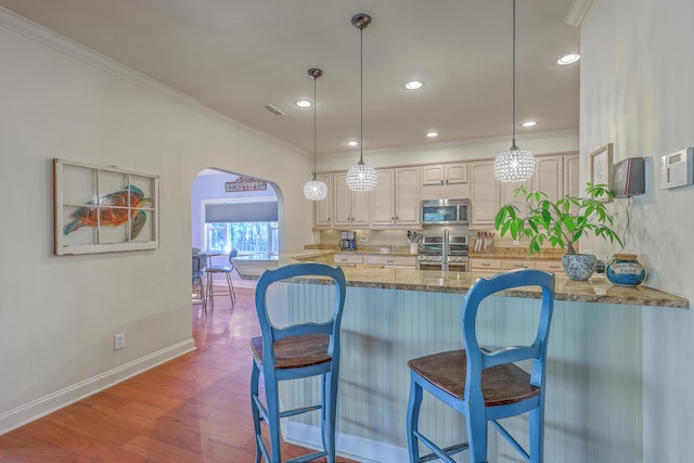 kitchen featuring arched walkways, appliances with stainless steel finishes, crown molding, and wood finished floors