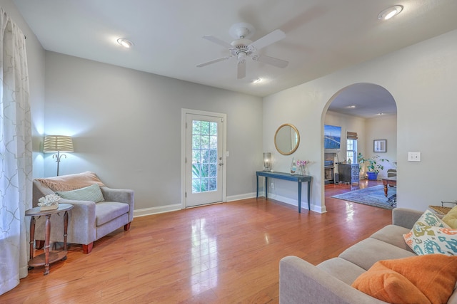 living room with light wood-type flooring, a ceiling fan, recessed lighting, arched walkways, and baseboards