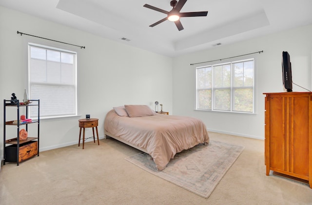 bedroom featuring ceiling fan, a raised ceiling, and light carpet