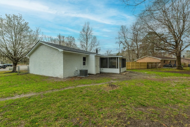 rear view of house with central AC unit, a sunroom, fence, a yard, and brick siding