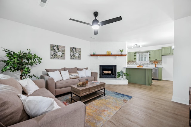 living room featuring visible vents, baseboards, ceiling fan, light wood-type flooring, and a brick fireplace