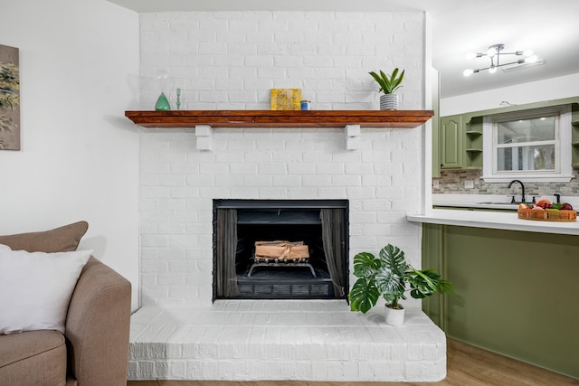 details with a brick fireplace, decorative backsplash, a sink, and wood finished floors