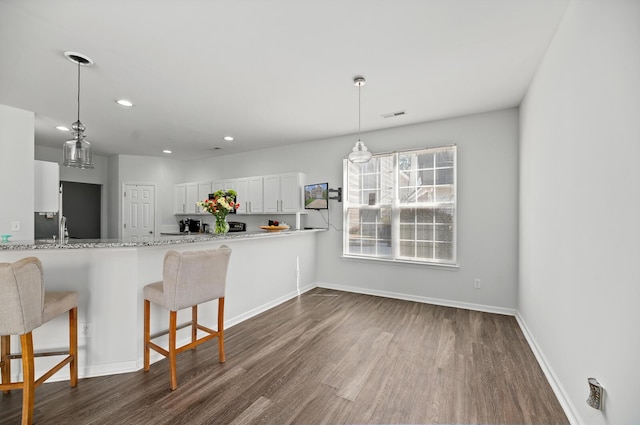 kitchen featuring visible vents, baseboards, dark wood-type flooring, white cabinetry, and a kitchen breakfast bar