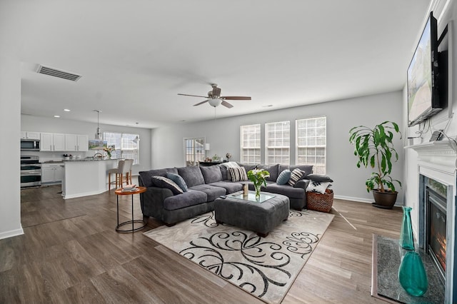 living area featuring baseboards, visible vents, a ceiling fan, dark wood-type flooring, and a fireplace