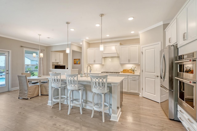 3173 Hugh Bennett Dr, Johns Island, SC 29455 - kitchen featuring stainless steel appliances, light wood-style floors, custom exhaust hood, a breakfast bar area, and ornamental molding