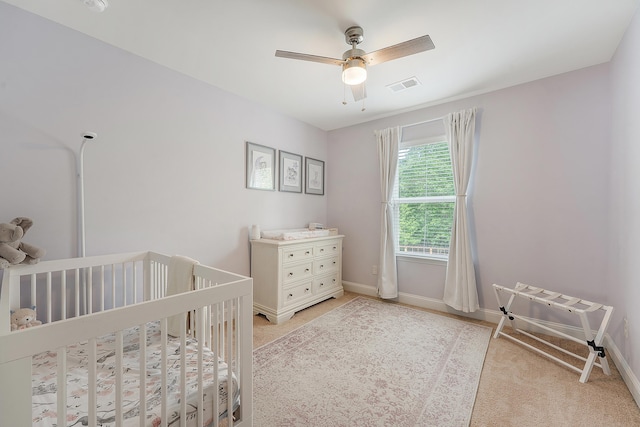 bedroom featuring a nursery area, baseboards, light colored carpet, and visible vents