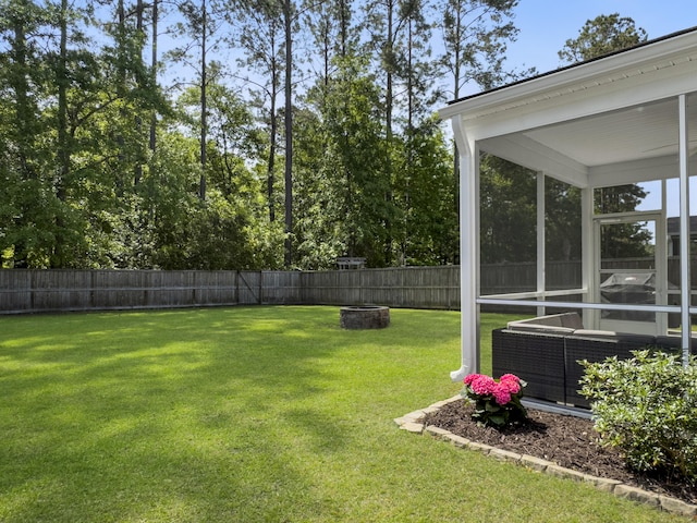 view of yard featuring a sunroom, a fenced backyard, and a fire pit