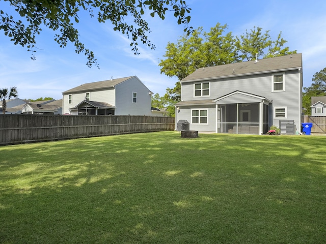 back of property with a lawn, a fenced backyard, a sunroom, and an outdoor fire pit