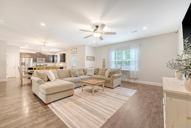 living room with light wood-style flooring, ceiling fan with notable chandelier, recessed lighting, baseboards, and visible vents