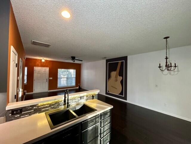 kitchen with dark hardwood / wood-style flooring, ceiling fan with notable chandelier, a textured ceiling, sink, and hanging light fixtures