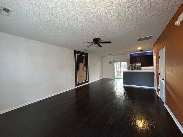 unfurnished living room featuring a textured ceiling, ceiling fan, and dark wood-type flooring