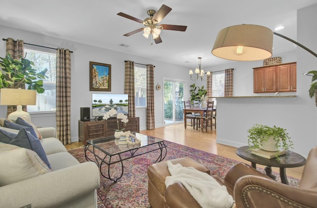 living room with light wood-type flooring and ceiling fan with notable chandelier