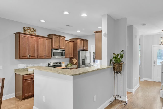 kitchen featuring light stone countertops, appliances with stainless steel finishes, light hardwood / wood-style floors, kitchen peninsula, and a breakfast bar