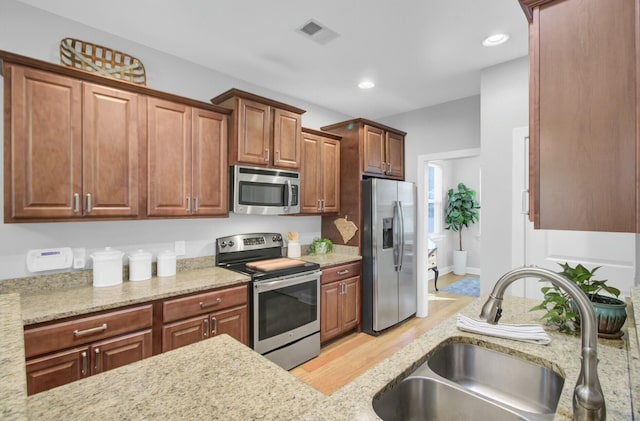 kitchen featuring stainless steel appliances, light hardwood / wood-style floors, light stone counters, and sink