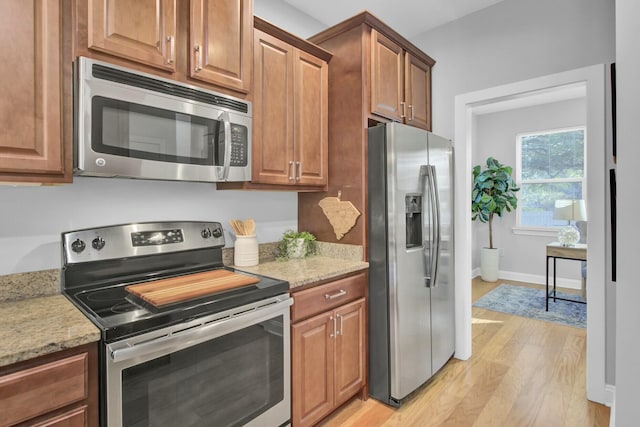 kitchen with appliances with stainless steel finishes, light stone counters, and light hardwood / wood-style floors