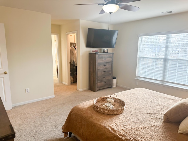 bedroom with a spacious closet, light colored carpet, ceiling fan, and a closet