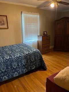 bedroom featuring wood-type flooring, ornamental molding, and ceiling fan