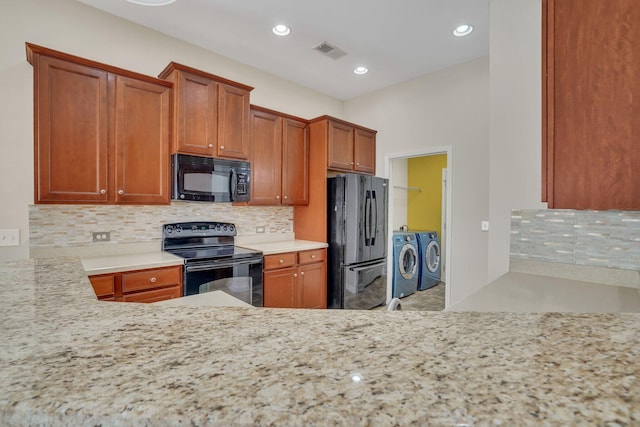 kitchen featuring washing machine and clothes dryer, decorative backsplash, light stone countertops, and black appliances