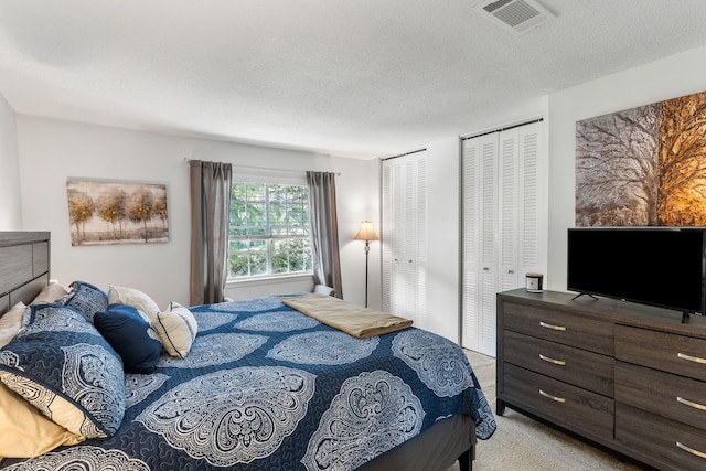 bedroom featuring multiple closets, a textured ceiling, and light colored carpet