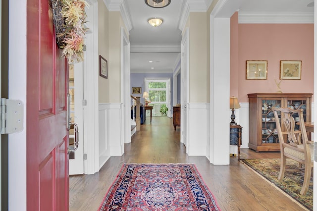 foyer featuring wood finished floors, ornamental molding, wainscoting, and a decorative wall