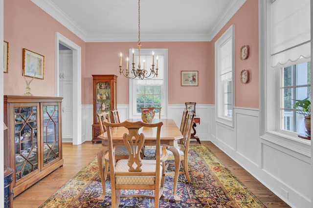 dining space featuring plenty of natural light, a chandelier, light wood-style flooring, a wainscoted wall, and ornamental molding