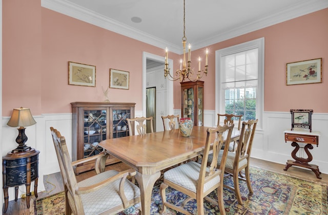 dining space featuring wood finished floors, ornamental molding, a wainscoted wall, a chandelier, and a decorative wall