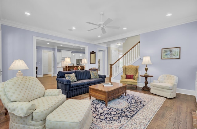 living room with wood finished floors, a ceiling fan, baseboards, stairway, and crown molding