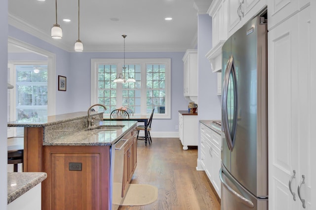 kitchen featuring stainless steel appliances, a sink, wood finished floors, light stone counters, and white cabinets