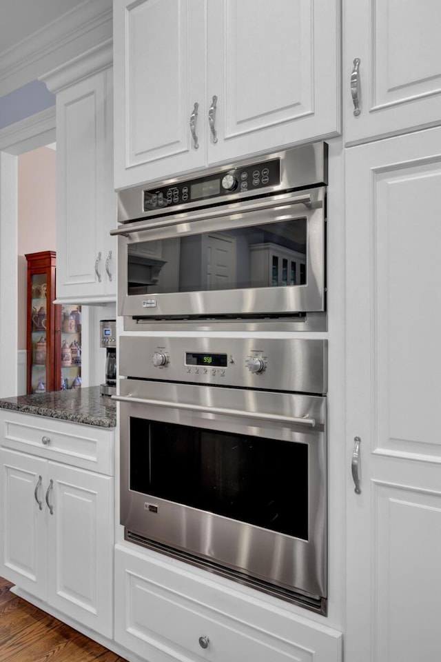 kitchen featuring white cabinets, stainless steel double oven, wood finished floors, and dark stone counters