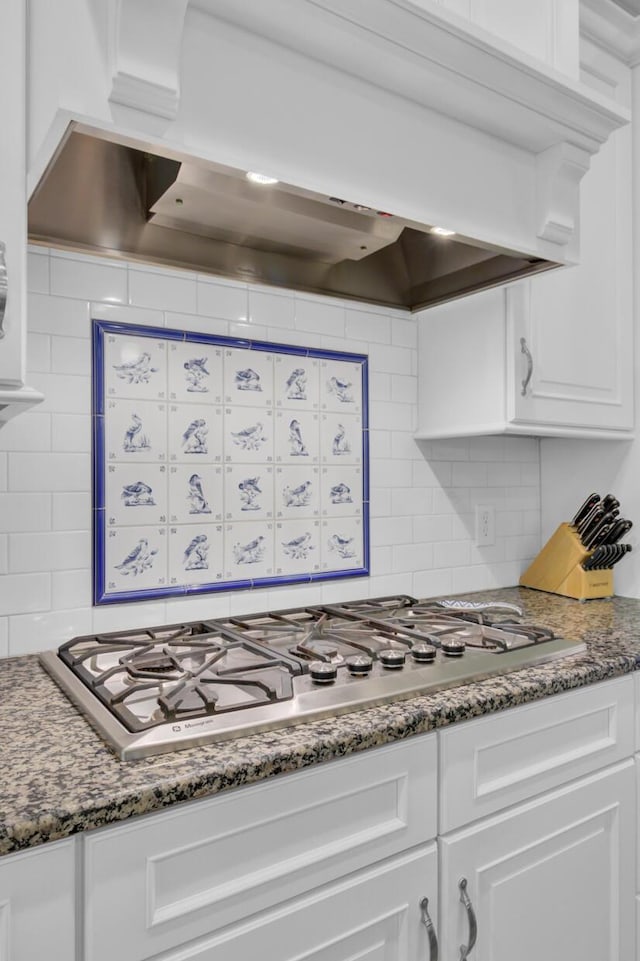 kitchen with stainless steel gas cooktop, custom exhaust hood, white cabinets, and decorative backsplash