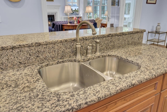 kitchen view of a sink, light stone counters, a tiled fireplace, and brown cabinets